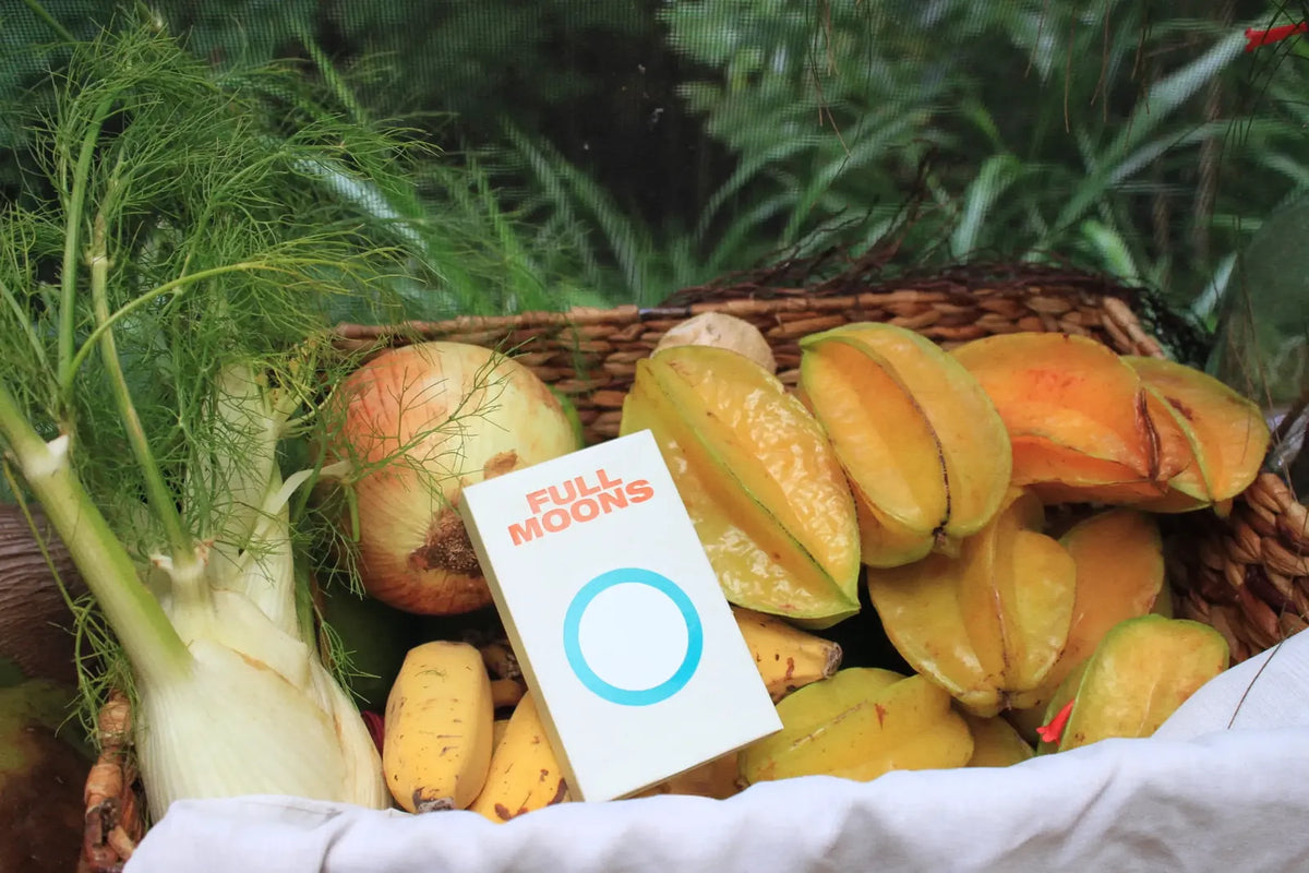 A pack of Full Moons resting in a basket of star fruit, bananas, onion and fennel outdoors