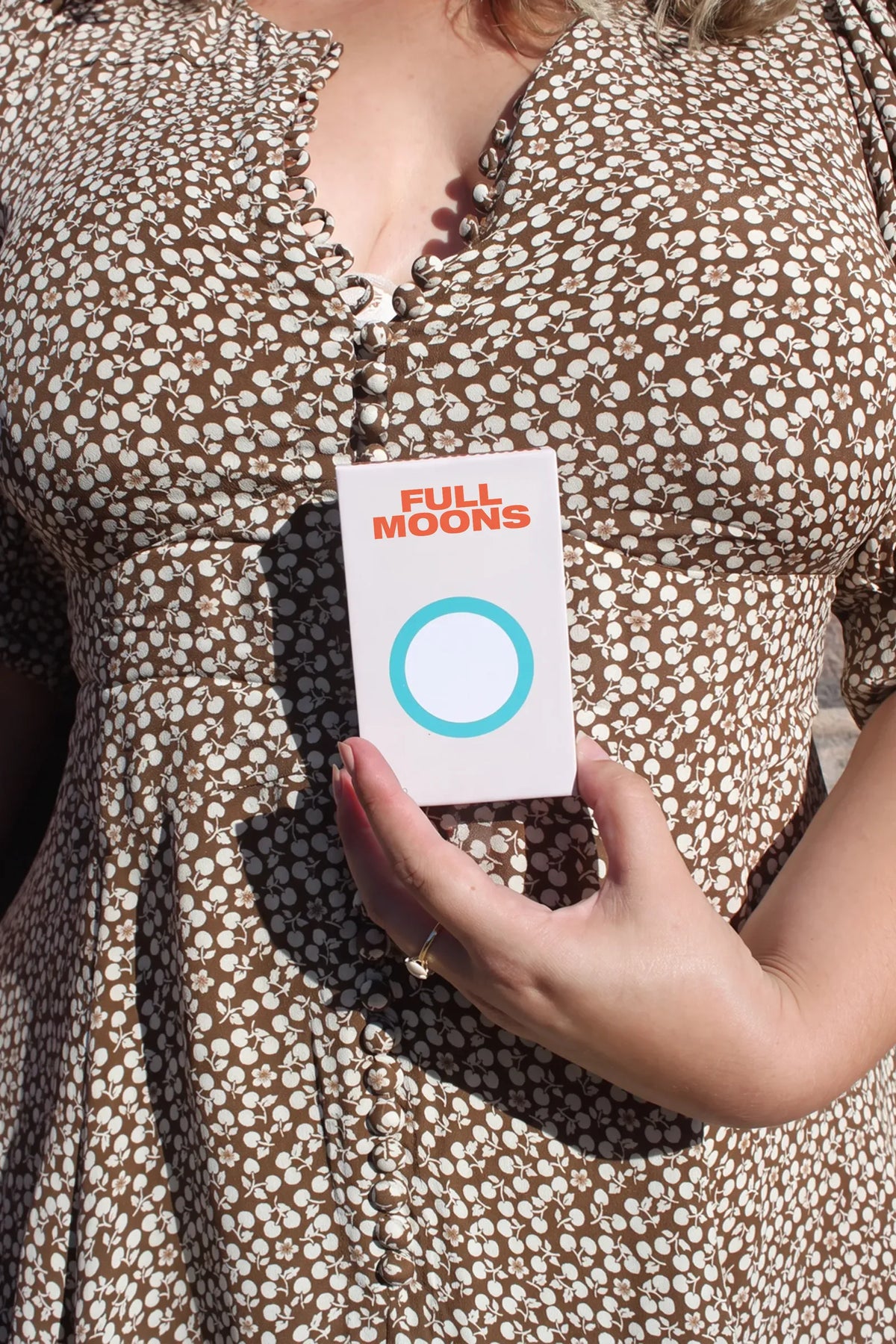 A woman in a brown floral dress holding a pack of Full Moons