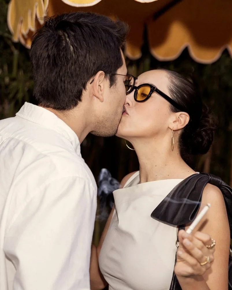 Two people kissing under a striped umbrella, one holding a Full Moons smoke