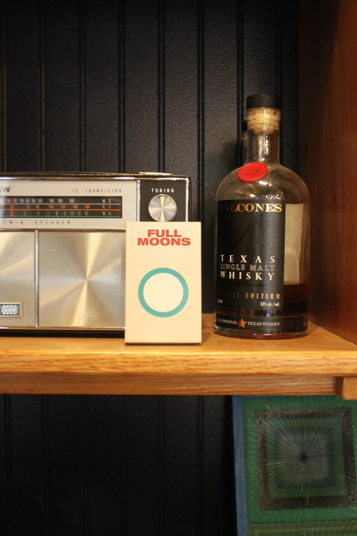 A pack of Full Moons on a wooden shelf between a vintage radio and a bottle of whisky