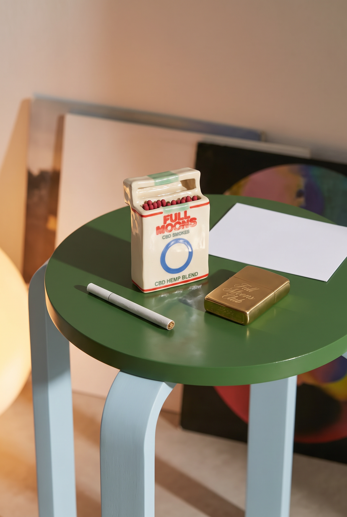 The Memento ceramic matchbox in Original on a green side table with a hemp cigarette and a brass Full Moons Club lighter